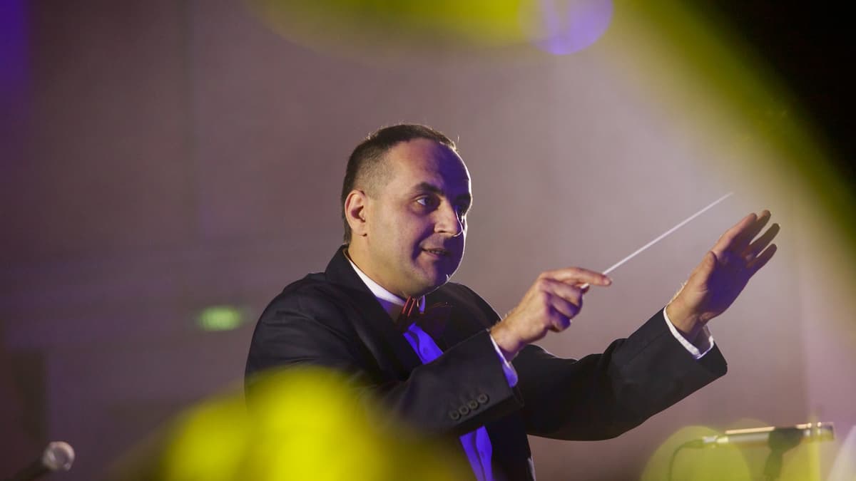 Conductor leading an orchestra with baton under stage lighting